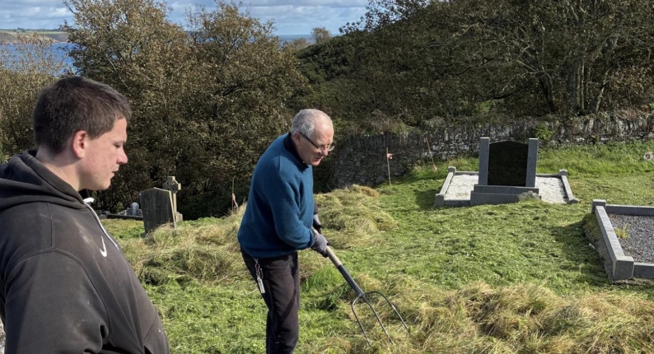 two men spread green hay on Ardmore graveyard floor